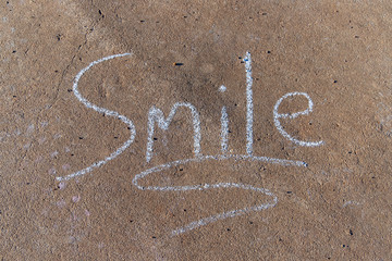 the word Smile written with sidewalk chalk on gray concrete background