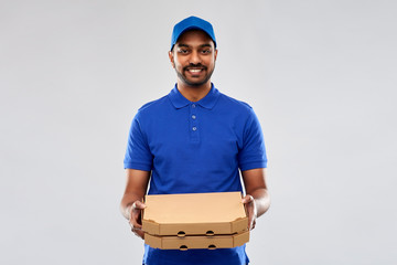 service and people concept - happy indian delivery man with pizza boxes in blue uniform over grey...