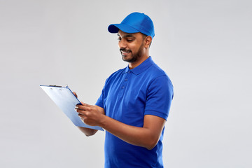 mail service and shipment concept - happy indian delivery man with clipboard in blue uniform over grey background