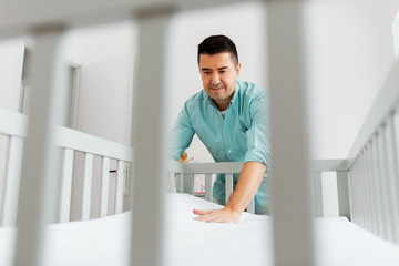 parenthood, fatherhood and nursery concept - middle-aged father arranging baby bed with mattress at home