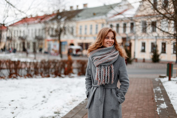Urban pretty young woman with a beautiful smile in a gray stylish coat in a knitted warm scarf...