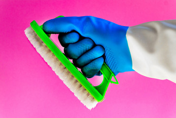 Hand with a blue rubber glove holding a green brush isolated on pink background