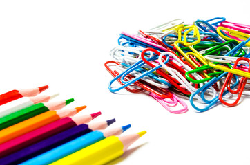 Many multi-colored stationery clips for documents and multi-colored pencils lie on a white background