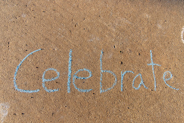 the word Celebrate written with sidewalk chalk on gray concrete pavement background