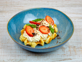 Belgian waffle with cream and strawberries in a blue plate