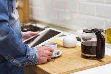 Hombre tomando un café en la cocina y mirando la tableta. Vista de frente y de cerca