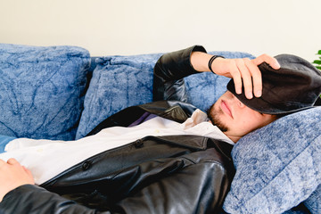 Young man tired of working makes a break for a nap on a sofa, wearing a hat.