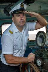 A sailor officer in the uniform is steering the ship with a rudder. Captain standing in the wheelhouse of ship and watching the surroundings. © milkovasa