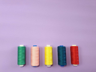 Colored sewing thread on a frosted purple fabric background, close-up.