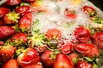 Strawberries in a bowl with water, washed to remove toxins and dirt before eating.