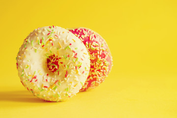 Obraz na płótnie Canvas Two colorful donuts on yellow background, closeup