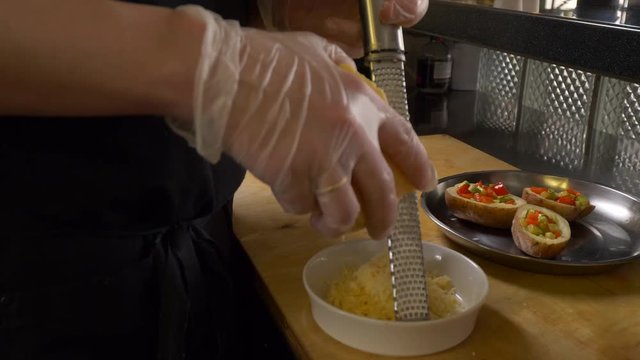 Process of cooking various delicious dishes in popular restaurant. Cook man rubs hard cheese on grater to sprinkle dish of potatoes with vegetables. Fish, meat, plate, pan, potato, cheese, shrimp