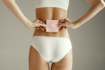Woman health. Female model holding empty card near back. Young adult girl with paper for sign or symbol isolated on gray studio background. Cut out part of body. Medical problem and solution.