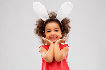 childhood, party props and easter concept - happy little african american girl wearing bunny ears...