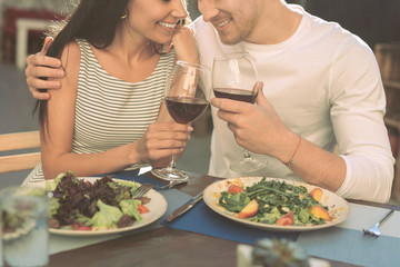 Strong handsome man hugging his skinny lady and clinking glasses with wine