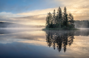 Scenic lake view with sunrise, island and foggy mood at beautiful autumn morning in Finland