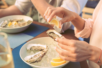 Woman with neat manicure squeezing lemon juice on fresh oyster