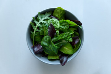 Bowl with mix fresh leaves of arugula, spinach and beet leaves on gray wooden background. Vegetarian food concept. Selective focus. Top view