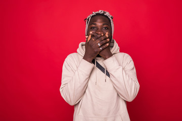 Young cool black man covering his mouth isolated on red background