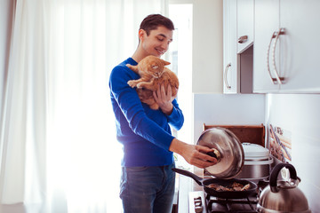 Portrait of handsome young man cooking with cat in the kitchen.