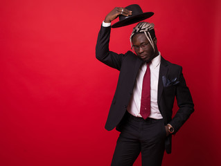 Fototapeta na wymiar Afro american business man in suit holding hat isolated on red background