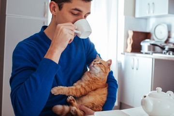 portrait of a young man drinking tea with a cat on kitchen
