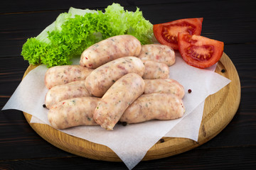 Fresh raw sausage with lettuce and tomato on the wooden background