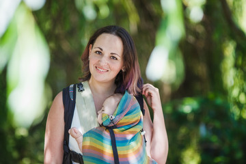Informal mother carry baby girl in baby carrier in park