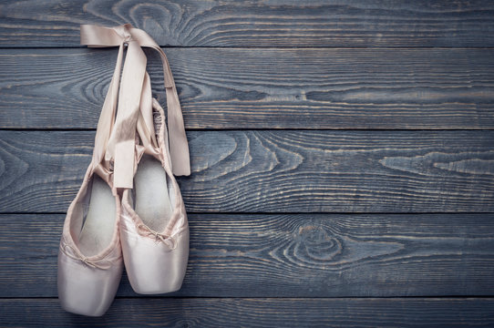 Pointe shoes ballet dance shoes with a bow of ribbons hang on a nail on a wooden background.