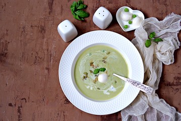 Cream of green pea soup, sprinkled with pumpkin seeds, in a white plate. Served with mozzarella cheese. Top view.