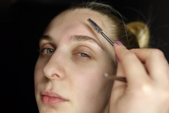  Beautician depilating a woman's eyebrows with tweezers on a black isolated background