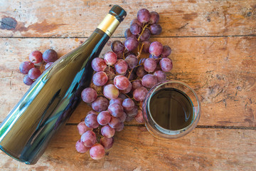 Bottle of red wine, grapes and glass of wine top view on the rustic wooden background