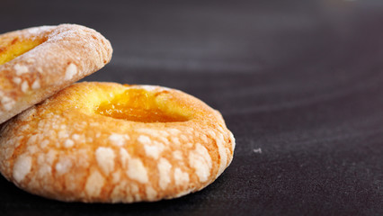 Two donuts with apricot jam on the left a black background. Delicious fresh pastry will be an addition to tea or coffee in a friendly company.