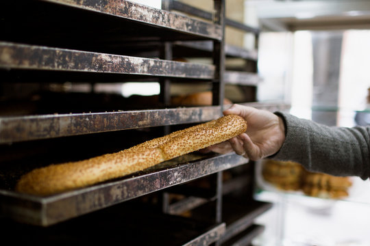 Hand Placing Fresh Sesame Bread Stick on Bakery Rack