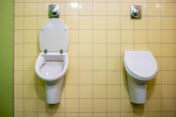 Two modern urinals in the men's toilet, one open, the other closed with a lid.