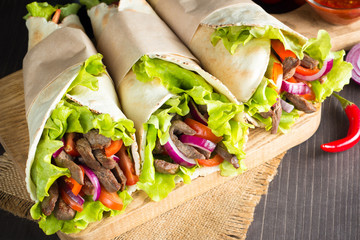 Photo of Mexican sandwich food, burrito, fajita, tacos, wrap made of tortilla, beef, chicken, fresh vegetables on rustic wooden background. Fast food concept. Healthy lunch snack. Copy space. 