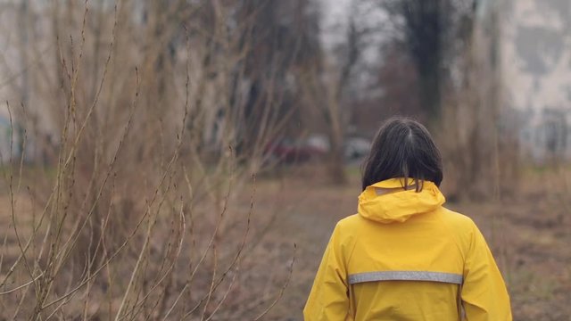 Rear view of woman in raincoat looking into distance on cloudy rainy winter day, slow motion handheld footage