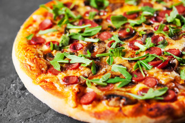 Pizza with Mozzarella cheese, mushrooms, ham, tomato sauce, sausage, pepper, Spices and Fresh arugula. Italian pizza on Dark grey black slate background