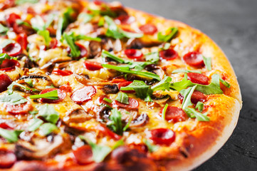 Pizza with Mozzarella cheese, mushrooms, ham, tomato sauce, sausage, pepper, Spices and Fresh arugula. Italian pizza on Dark grey black slate background