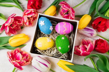 Obraz na płótnie Canvas Easter background with colorful knitted Easter eggs and tulip flowers on stone background. Easter background, handmade holidays decorations and gift concept. Top view