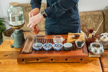 Chinese tea tasting in the tea shop. Tea seller, dressed in European, brews Chinese tea for tasting. Chinese tea set, close-up traditional Chinese teapot and cups on bamboo mats