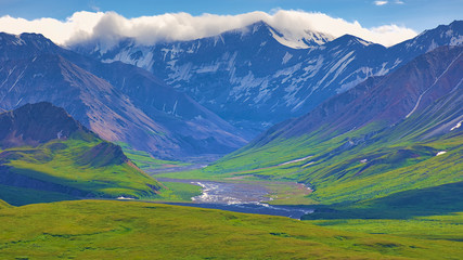 Fototapeta na wymiar With its huge mountains and surrounded by a wonderful biodiversity lies the Denali National Park and Preserve. River, field and cloud sky. Landscape, fine art. Parks Hwy, Alaska, EUA: July 28, 2018
