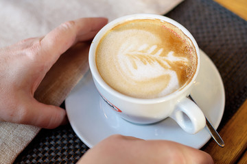 Cup of cappuccino with latte art. Beautiful foam, white cups. Hands in shot.