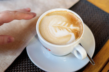 Cup of cappuccino with latte art. Beautiful foam, white cups. Hands in shot.