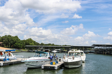 Fototapeta na wymiar Luxury speedboats fueling up at gas pump at marina on lake with docks and boats behind under beautiful blue cloudy sky