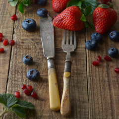 Mixed berries, blueberry, strawberry on wood background with vintage, styled fork and knife. Styled food, fruit background. Template for social media.