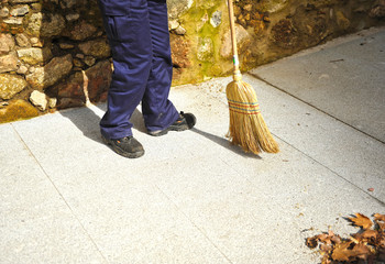 Sweeper sweeping the autumn leaves on town sidewalk. Municipal cleaning worker 