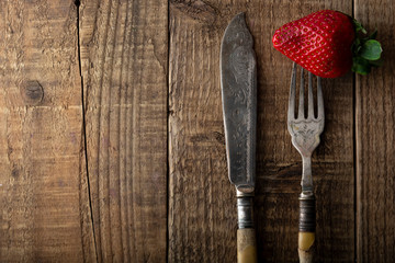 Eating fresh strawberries, vintage cuttlery fork and knife. Healthy diet and slim figure, breakfast or healthy snack. Detox and loose weigh. Textured, rustic wooden table.