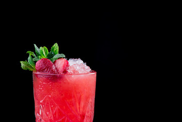 Beautiful red berry cocktail with ice, decorated with fresh berries and mint,   isolated on a black background. Close-up. Space