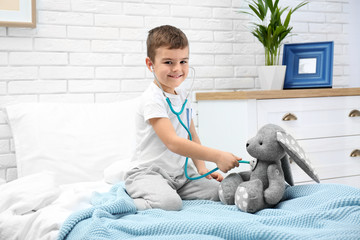 Cute child playing doctor with stuffed toy on bed in hospital ward
